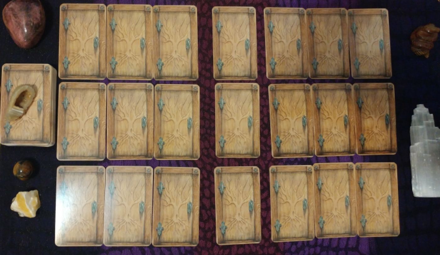 Twenty-one matching cards (faced-down) that resemble unopened wooden doors, hinting at the unknown. The frame of each door is of a darker wood, two pentagrams etched in the top corners. A naked tree is etched into the door with the roots reaching down towards the earth, the branches reaching towards the sky; this encompasses the three realms of the deep influences of the past, the present moment, and the influences from above. The cards are sectioned off in a grid-like pattern. Three cards represent each of the following categories: romantic life, social life, finances, aspirations, positive influences, and negative influences. Between romantic/social lays a card representing the balance between the two. Between finances/aspirations lays a card representing the balance between the two. Between positive/negative influences lays a card representing the balance betwen the two. To the left of the spread lays a piece of polished rhodenite (for love), tawny-colored banded agate (for protection) laying on the remainder of the deck, polished sphere of hawk's eye (for insight), and a piece of raw, yellow calcite (self-confidence and hope).